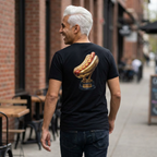 Man wearing a black t-shirt with a hot dog graphic on the back, walking down a street.