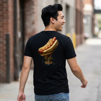 Man wearing a black t-shirt with a gold hot dog graphic on the back, walking down a street.